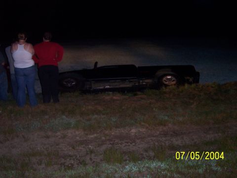 1994 Ford Bronco - Pickup truck overturned on the side of the road at night with onlookers.