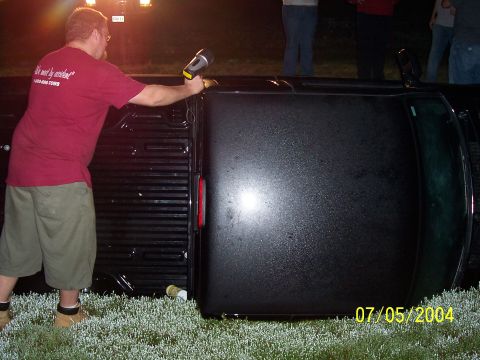 1994 Ford Bronco - A black pickup truck lies on its side in the grass, illuminated by a flashlight.