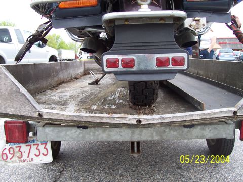 1994 Ford Bronco - A motorcycle is loaded onto a trailer, with a white truck visible in the background.