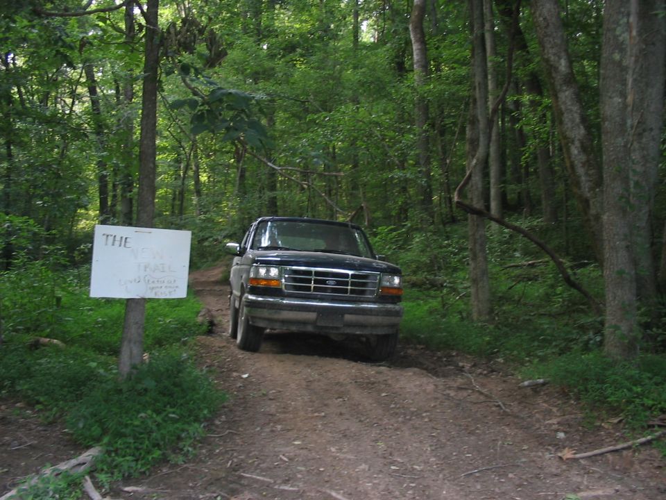 Dark SUV on dirt road with a sign that says "THE NEW TRAIL"