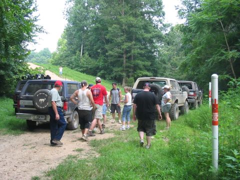 1988 Ford Bronco - Several Ford Broncos are parked on a dirt path surrounded by trees, with a group of people standing nearby.