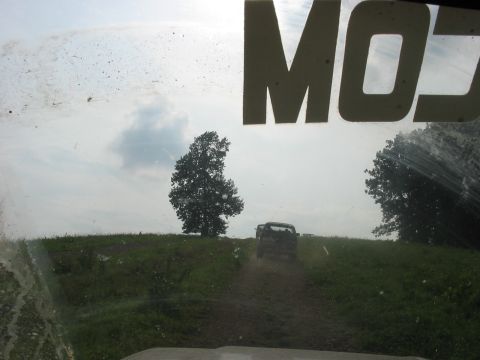 1988 Ford Bronco - View from inside a vehicle as another SUV drives up a muddy hill, with large white lettering visible on the windshield.