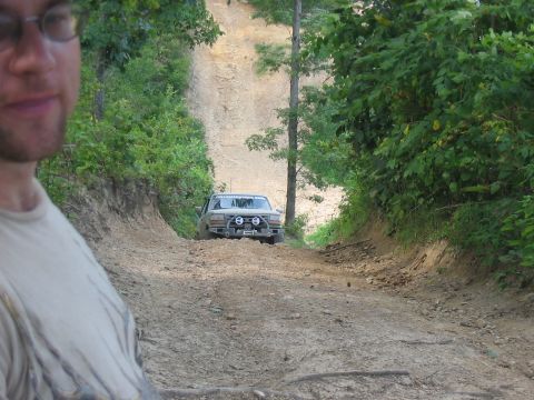 1988 Ford Bronco - A tan 1987 Ford Bronco navigates a steep, muddy incline surrounded by dense foliage.