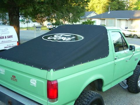 1990 Ford Bronco - A green Ford Bronco shown from the rear three-quarter angle with the hardtop removed and a black soft top installed featuring a white Ford…