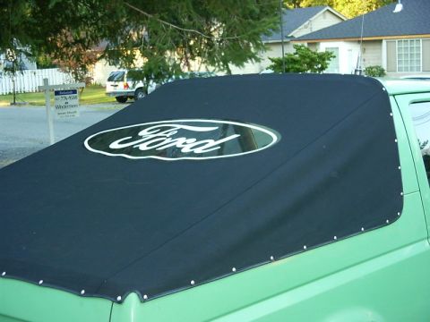 1990 Ford Bronco - Close-up of a green Ford Bronco fitted with a black soft top featuring a white oval 'Ford' logo and metal snap fasteners around the edges.…