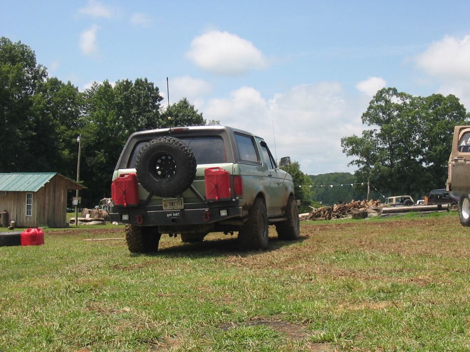 Rear view of a green 1988 Ford Bronco with a spare tire and two red gas cans mounted on the back