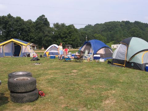 1995 Ford Bronco - A campsite scene with multiple tents set up, people relaxing, and a stack of tires in the foreground.