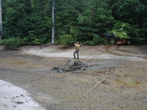 1993 Ford Bronco - A person celebrates atop a mud-covered buggy in a dry lake bed, with other vehicles visible in the trees.
