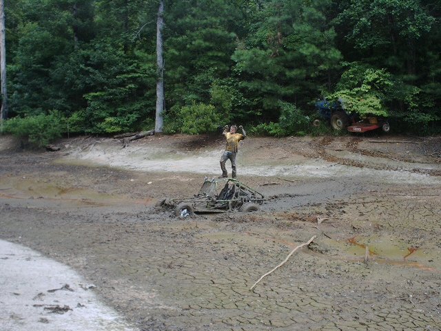 Guy standing on a muddy off-road buggy stuck in a dry lake bed, other vehicles in background