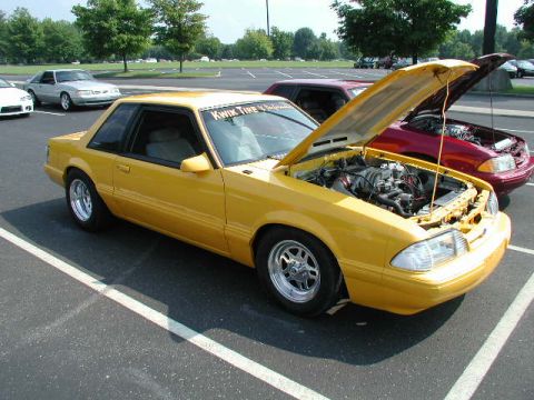 1998 Ford Crown Victoria - Yellow coupe with hood open, parked in a lot next to other vehicles.