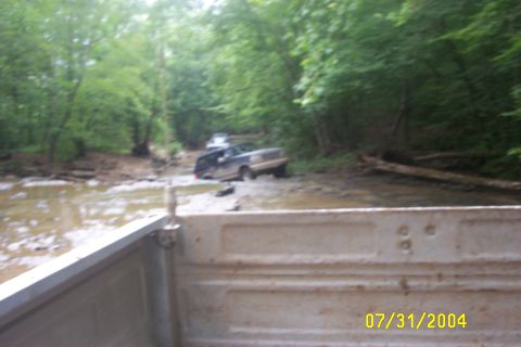 1979 Ford F-150 - Two trucks are stuck in a muddy creek bed surrounded by trees, with a date stamp of 07/31/2004.