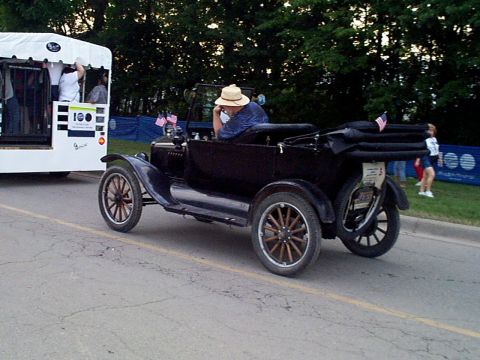 1999 Ford Taurus - A vintage black convertible with a straw-hatted driver passes a white trailer during a parade.