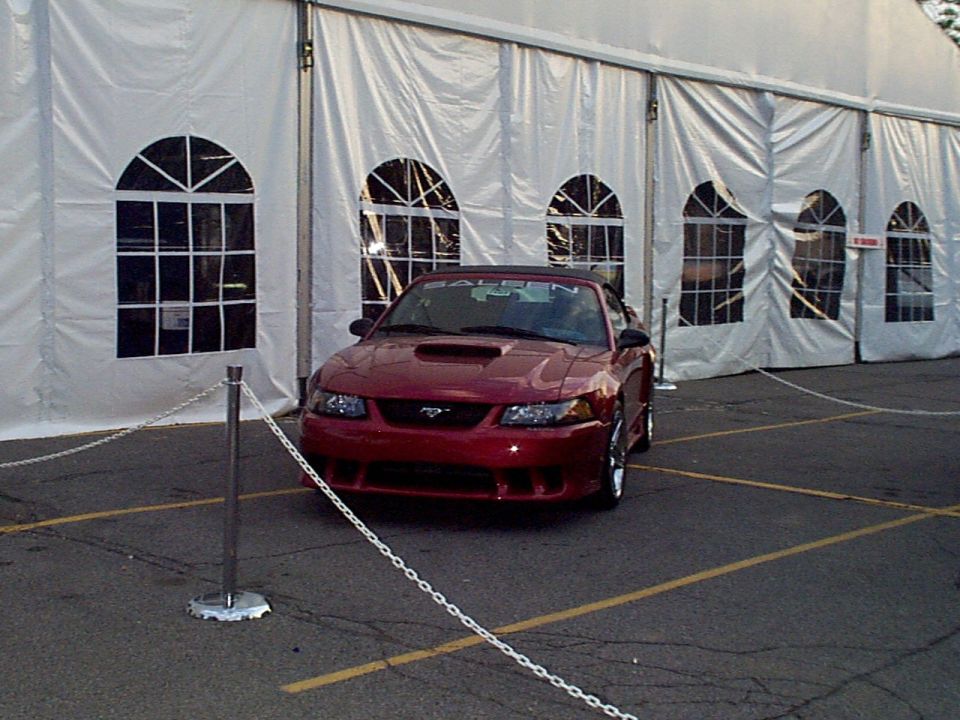 Dark red Saleen Mustang convertible roped off with chain stanchions in front of a white event tent