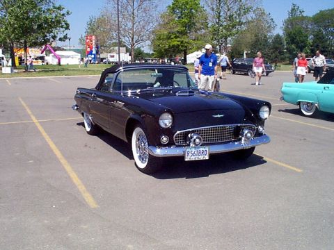 1999 Ford Taurus - A classic black Ford Thunderbird convertible is parked in a lot, with a teal car visible to its right.