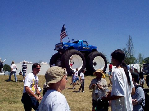 1999 Ford Taurus - A blue monster truck with a Ford logo and 'BIGFOOT' text is on display with spectators around it.