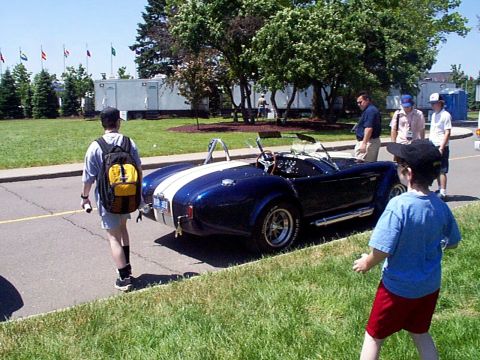 1999 Ford Taurus - A blue convertible sports car with white racing stripes is parked on the side of the road, attracting attention from onlookers.