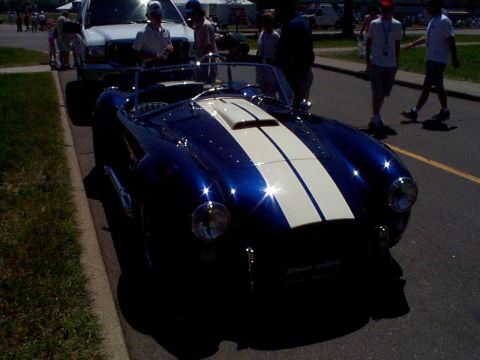 1999 Ford Taurus - A blue convertible sports car with white racing stripes is parked on the side of a street.