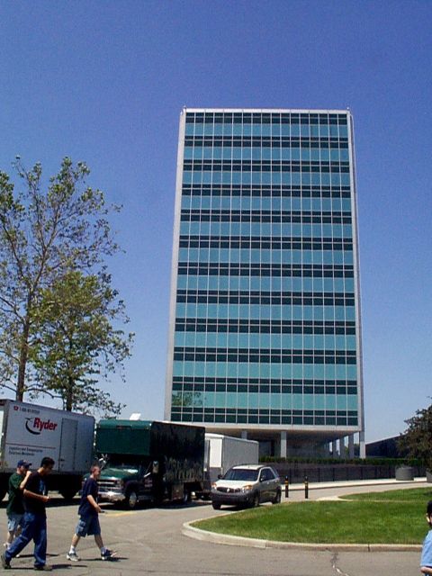 1999 Ford Taurus - A modern office building stands tall against a clear blue sky, with several vehicles parked in the foreground.
