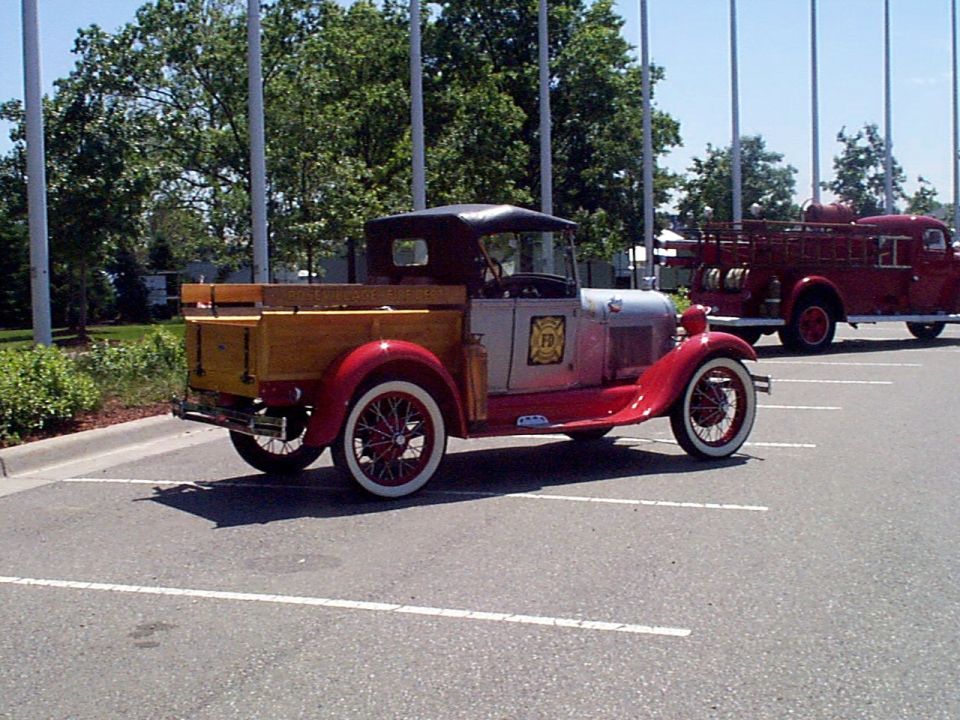 Antique red and silver pickup truck with wooden bed parked next to a red fire truck