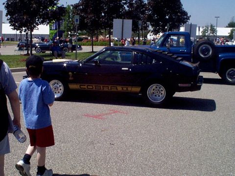 1999 Ford Taurus - A classic Ford Mustang Cobra II is shown from the side, with a blue pickup truck in the background.
