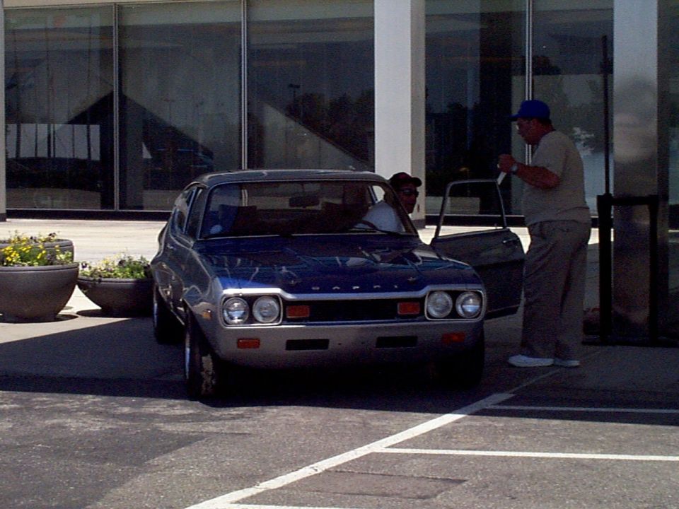 Blue hatchback car with dual headlights and chrome bumper parked outside a building
