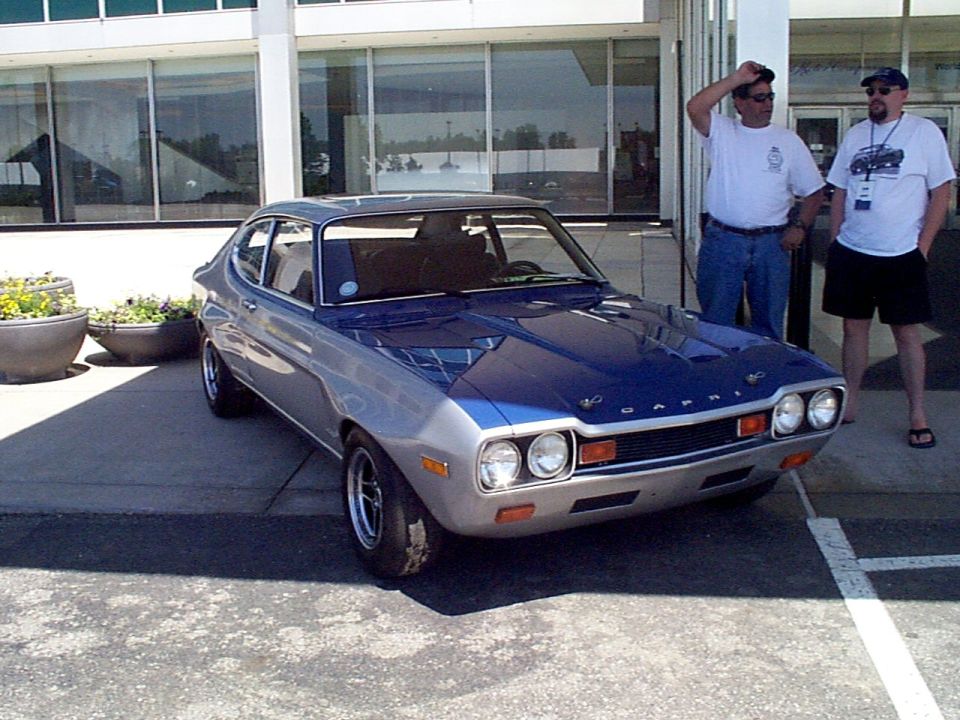 Blue and silver Ford Capri parked outside a building with two men standing nearby