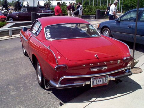 1999 Ford Taurus - A red Volvo P1800 coupe is parked next to a blue sedan, with people in the background.