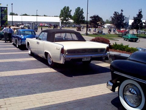 1999 Ford Taurus - A cream 1961 Lincoln Continental convertible is parked in a line of cars.