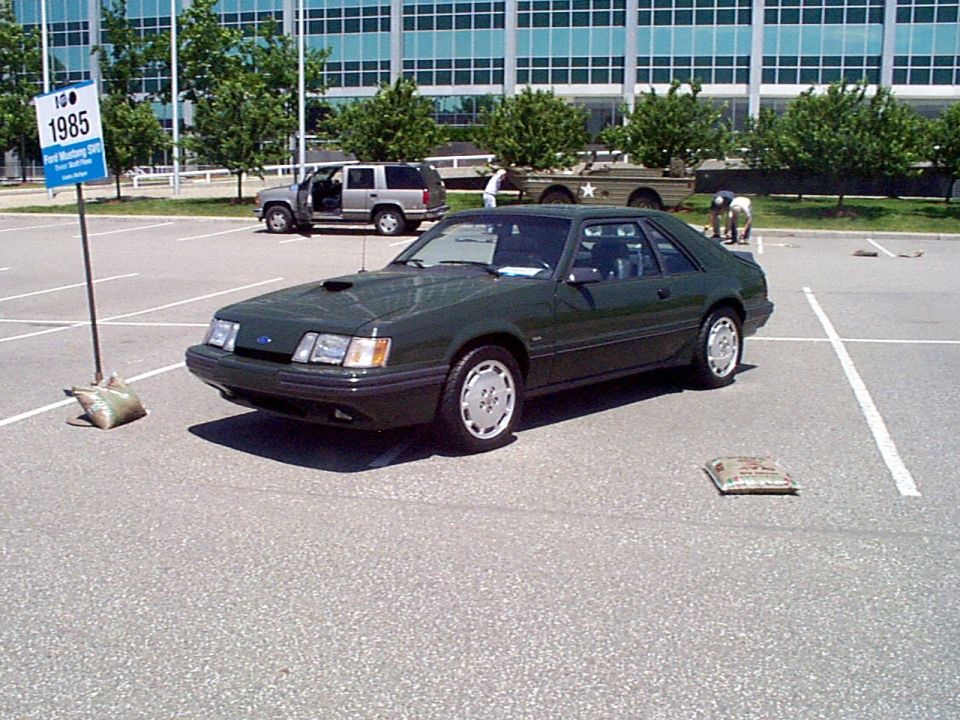 Dark green 1985 Ford Mustang coupe parked in a lot, front 3/4 view