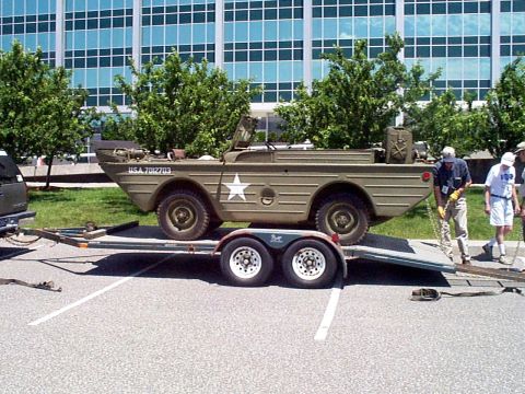 1999 Ford Taurus - An amphibious military vehicle, marked USA 7012703, is being loaded onto a trailer in front of a modern office building.