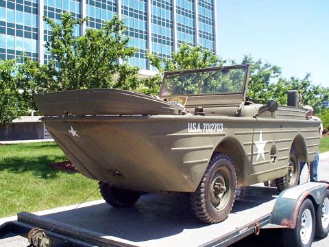1999 Ford Taurus - Olive drab amphibious vehicle with USA 7012703 marking on trailer in front of a modern building.