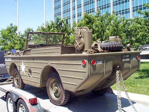 1999 Ford Taurus - This olive drab military amphibious vehicle, marked with '1942', is shown on a trailer in front of a modern building.