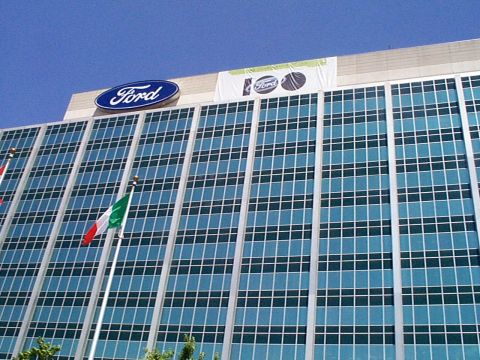 1999 Ford Taurus - Exterior view of a Ford building, a "100" anniversary banner and the iconic Ford logo against a clear blue sky.