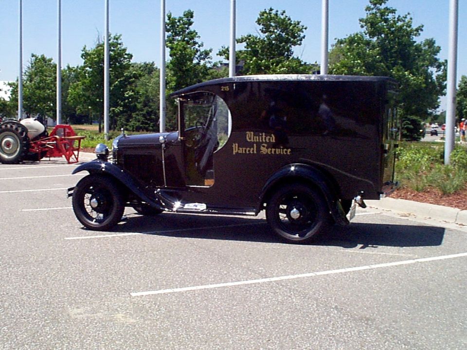 Brown United Parcel Service delivery truck parked in a lot, with a tractor in the background