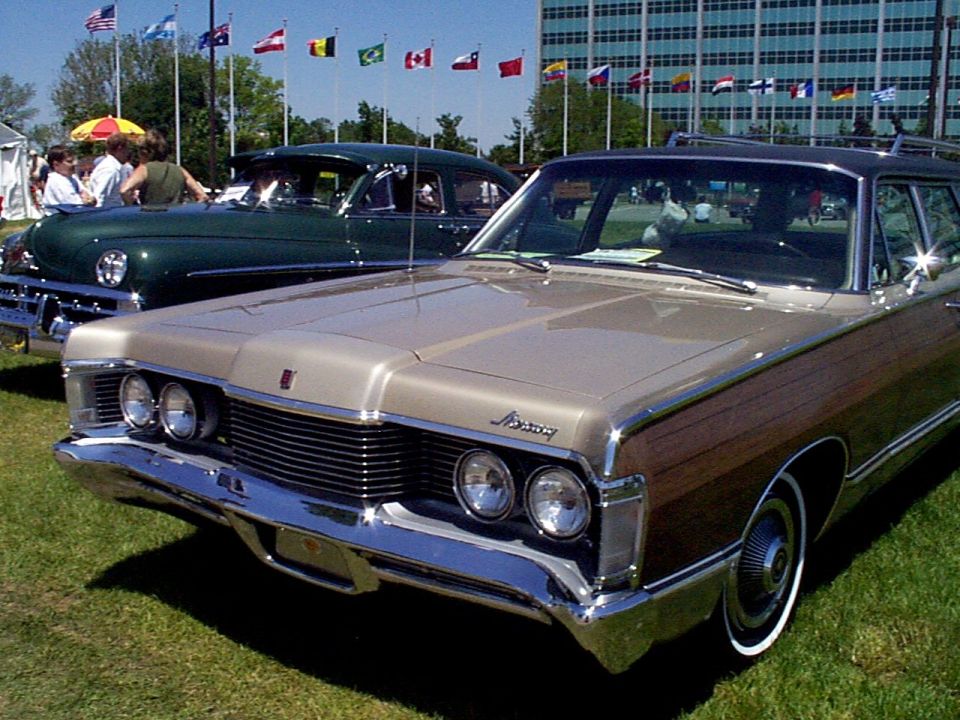 Wood-paneled Mercury station wagon, front end visible. Another classic car is parked behind it