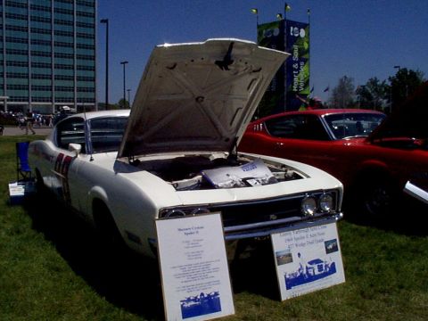 1999 Ford Taurus - A white 1969 Dodge Charger is displayed with its hood open, parked next to a red car.