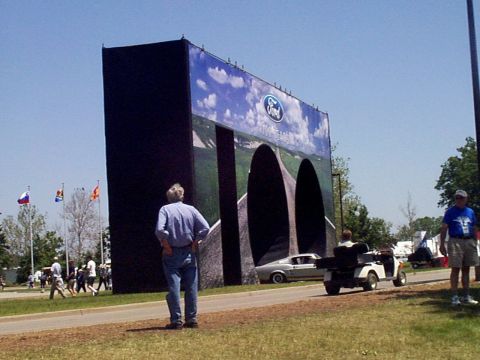 1999 Ford Taurus - A large Ford display features a classic silver car and a golf cart in front, with people milling about in the background.