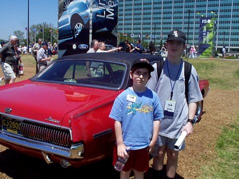 1999 Ford Taurus - A red 1969 Mercury Cougar is parked outside with two young boys standing beside it.