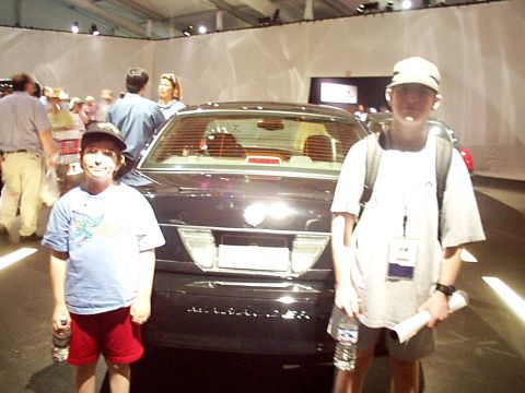 1999 Ford Taurus - A dark sedan is viewed from the rear, with two young boys standing in front of it.