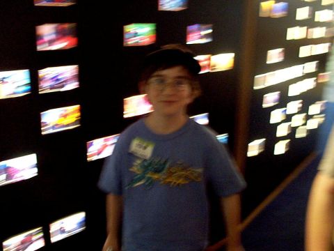 1999 Ford Taurus - A young boy wearing a blue t-shirt and glasses stands before a display of numerous small, glowing images on a dark wall.