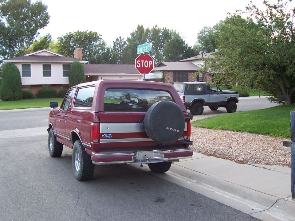 Red Ford Bronco rear with spare tire cover parked by a stop sign in a neighborhood