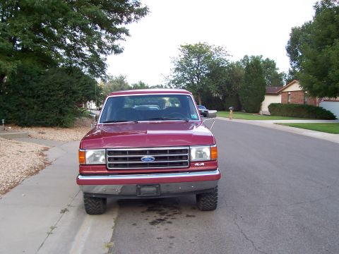 1991 Ford Bronco - Front view of a red 1991 Ford Bronco parked on a suburban street. The vehicle features a chrome grille and 4x4 badging.