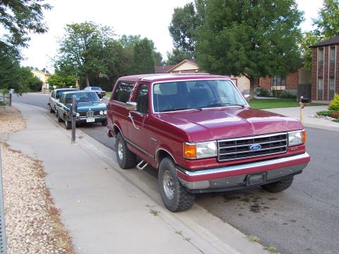 1991 Ford Bronco - Red 1991 Ford Bronco parked curbside on a sunny day, with other vehicles visible in the background.