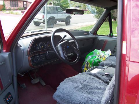 1991 Ford Bronco - Interior view of a red Ford Bronco, with another Bronco visible outside. The dashboard and steering wheel are prominent.