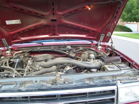 1991 Ford Bronco - Engine bay of a red 1991 Ford Bronco, showing the engine and surrounding components with the hood fully open.