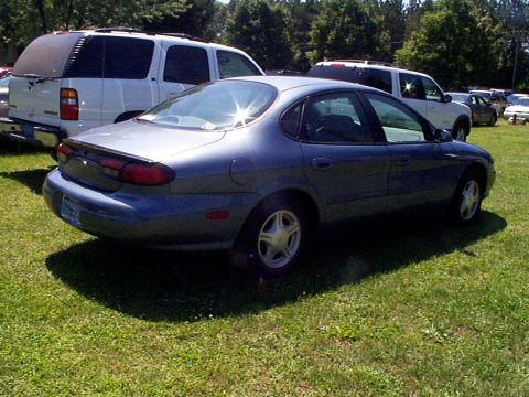 1999 Ford Taurus - A blue 1999 Ford Taurus SE is parked on a grassy area with other vehicles in the background.