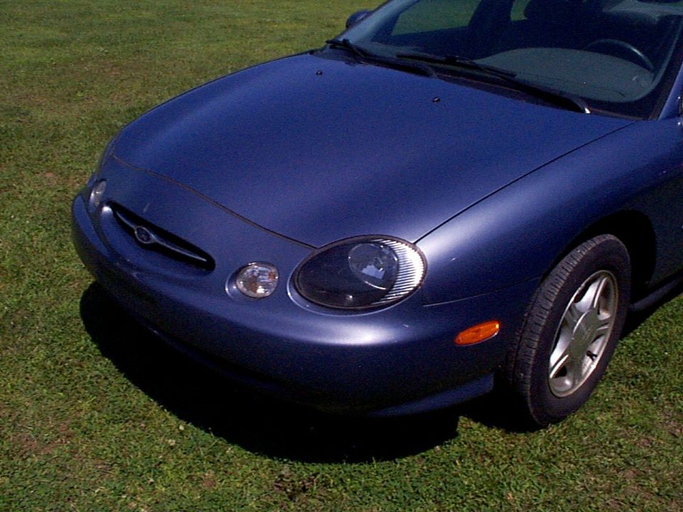 Front corner of a blue 1999 Ford Taurus parked on grass