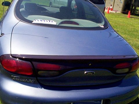 1999 Ford Taurus - The rear of a blue 1999 Ford Taurus SE is shown with a spoiler and tinted taillights.