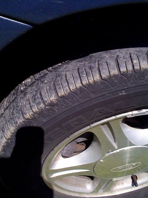 1999 Ford Taurus - A close-up view of a vehicle's tire and wheel assembly, showing a Ford emblem on the hubcap.