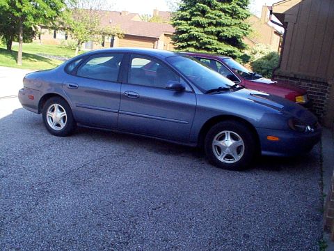 1999 Ford Taurus - A blue 1999 Ford Taurus SE is parked next to a red car in a driveway.